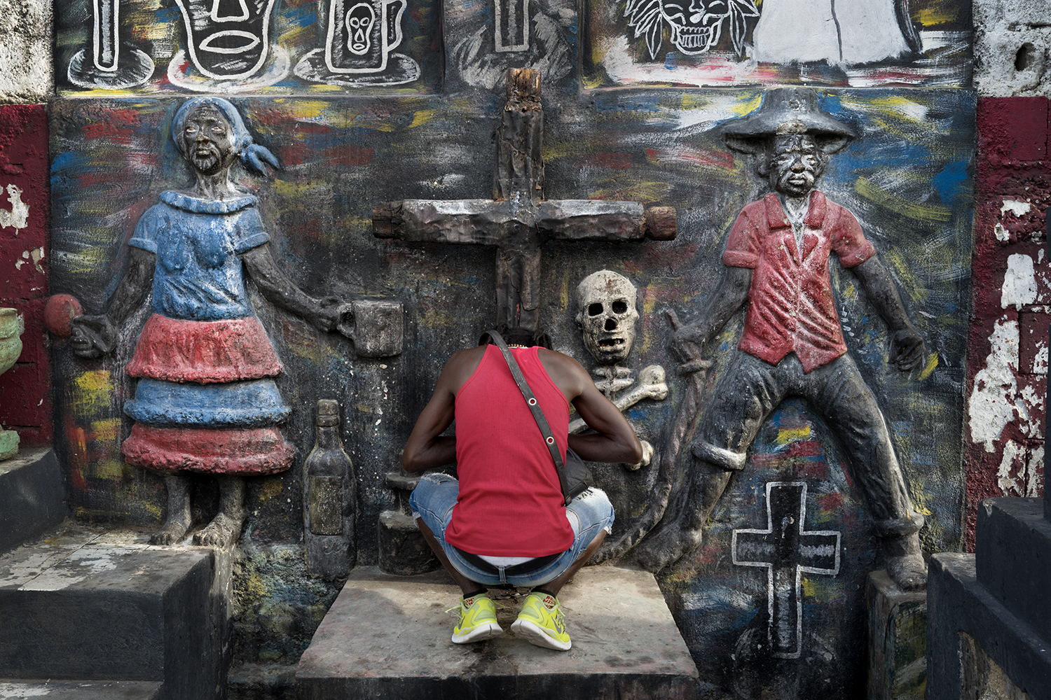 Le grand cimetière de Port au Prince est tenu par les gangs et plus aucun enterrement n'y est organisé. Ici, un membre du gang qui surveille le cimetière prie face à la croix du Lwa (esprit du panthéon vaudou) -Baron Criminel-. Tous les membres pratiquent le vaudou et croient fermement aux pouvoirs mystiques.