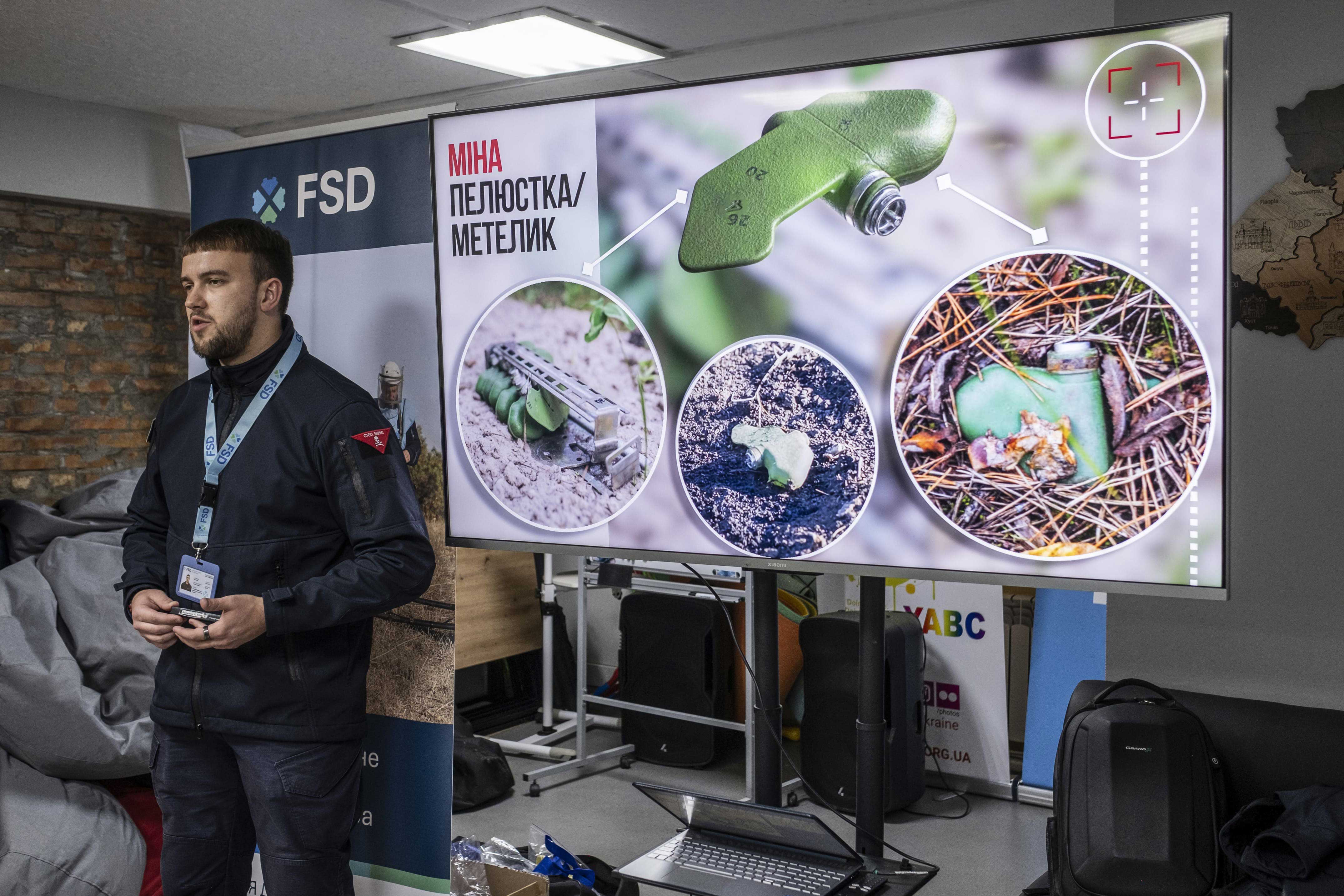 Ruslan, membre de l’équipe EORE (Éducation aux risques liés aux munitions explosives), explique le fonctionnement et les dangers liés aux mines PFM-1 (mines pétales) lors d’une session donnée à des élèves de 1re année secondaire du lyceum 3 d’Izioum, le 29 octobre 2025.