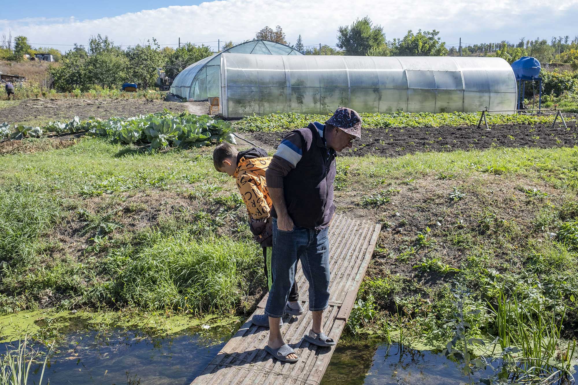 Sergii et son petit-fils de 13 ans, Bogdan, regardent s'il y a des poissons dans le ruisseau qui traverse le potager de Sergii et Paulina, le 25 septembre 2025.
