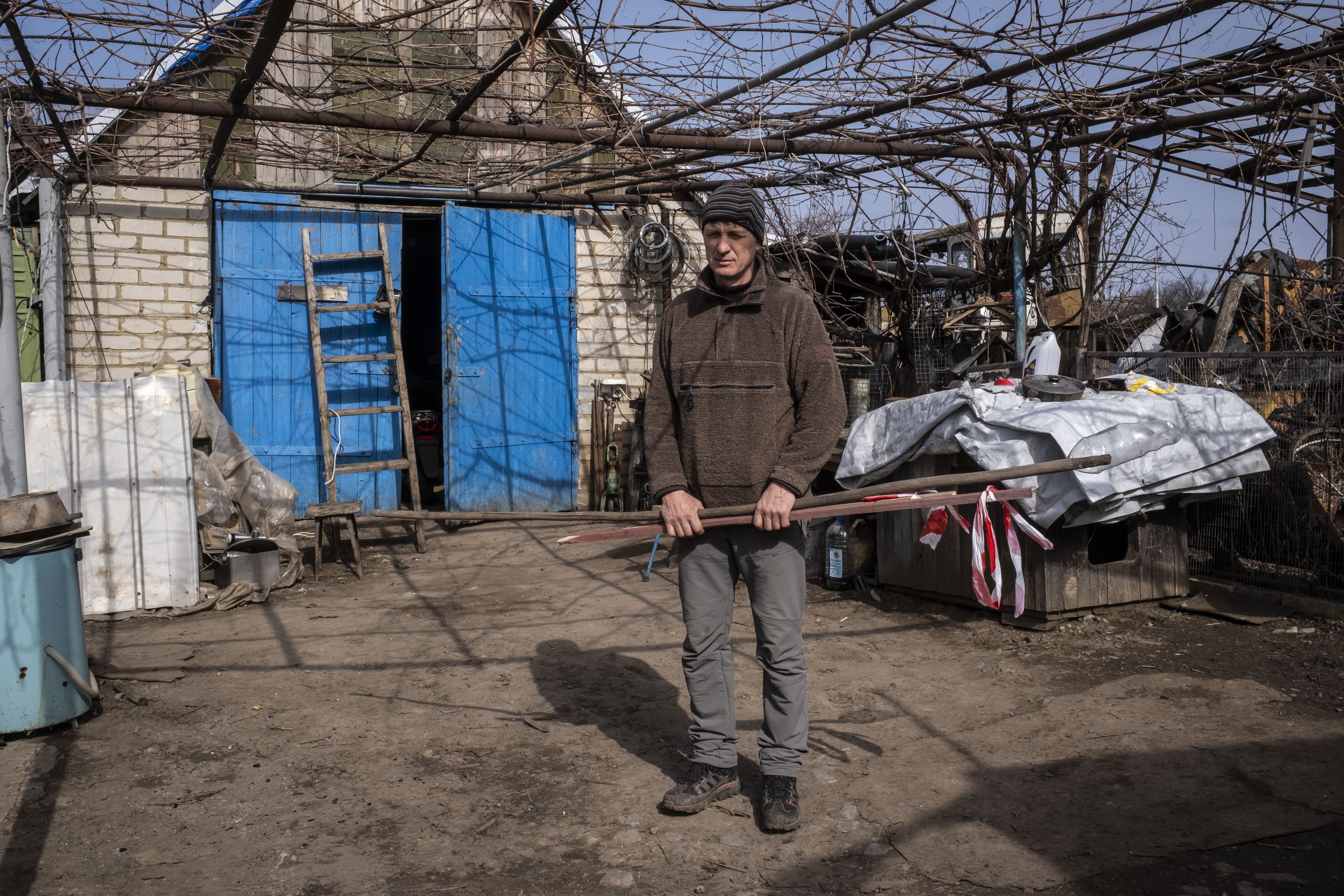 Volodymyr se prépare, le 16 mars 2026, à aller voir un de ses champs qui n'a pas encore été décontaminé et qu'il compte exploiter cette année. Dans ses mains, des bâtons pour indiquer où se trouvent les mines, ainsi qu'un bâton équipé d'une demi-bouteille d'eau pour ramasser d'éventuelles mines pétales.